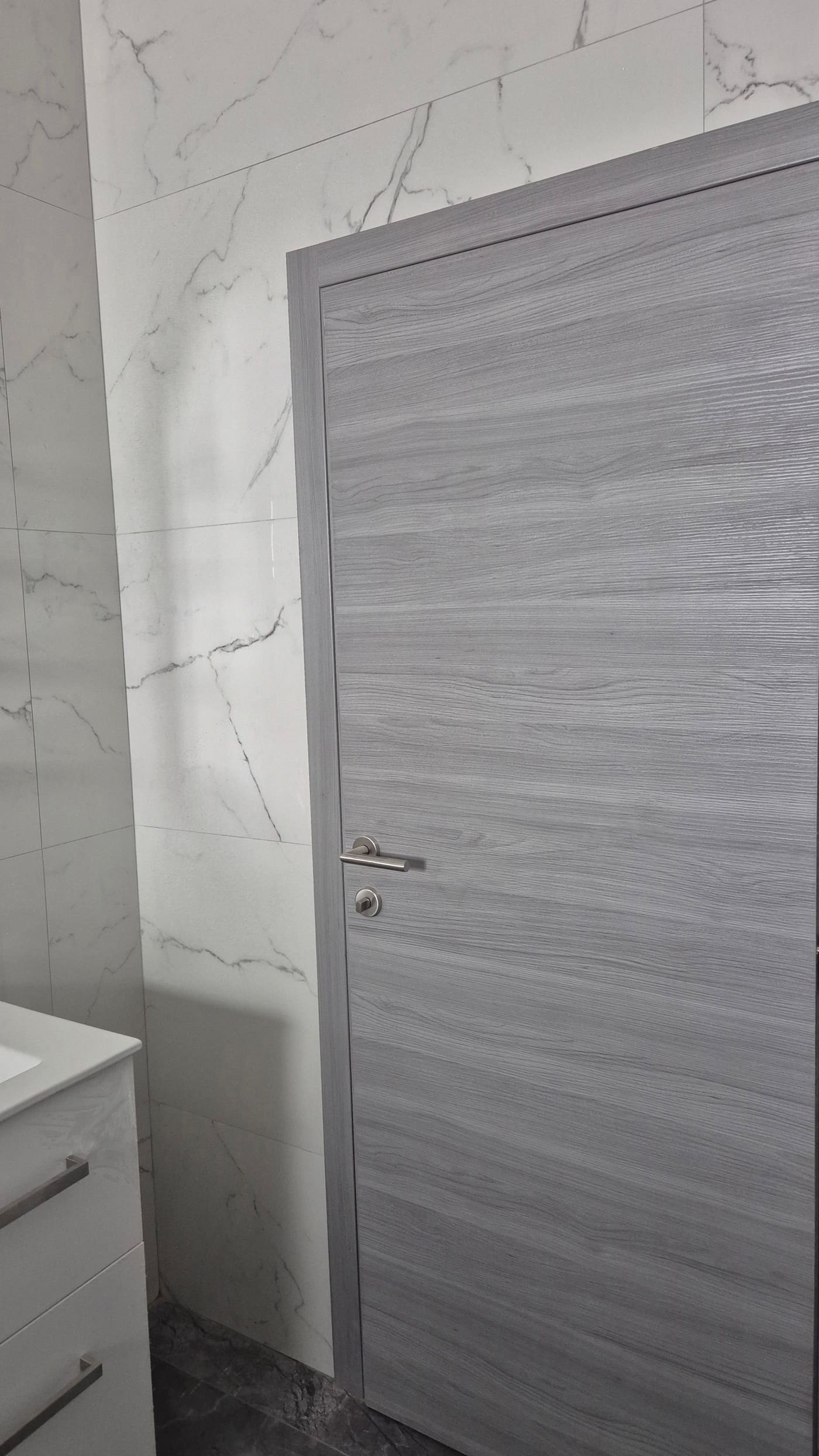 Siva laminirana vrata u kupaonici obloženoj mramornim pločicama